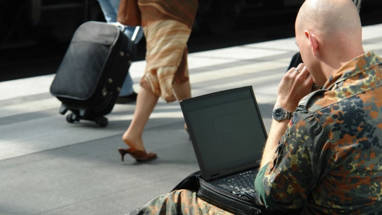 Mann in militärischer Kleidung arbeitet an einem Bahnsteig auf einem Laptop