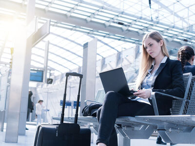 Eine Frau arbeitet am Laptop während sie am Bahnsteig wartet