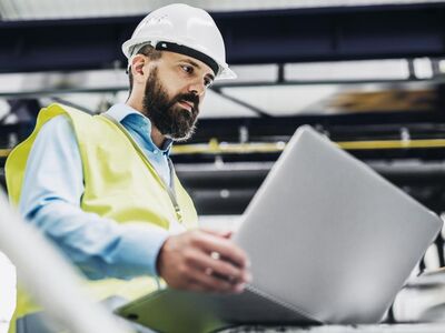 Man mit Schutzhelm schaut auf einen geöffneten Laptop